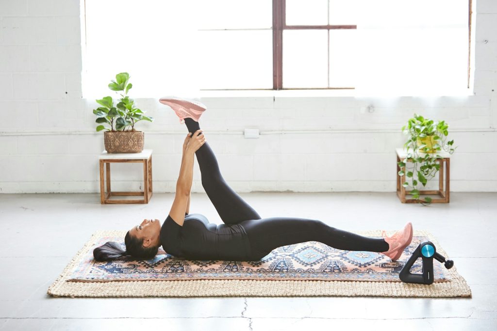 woman in black tank top and black leggings lying on black and white floral area rug. total body stretch